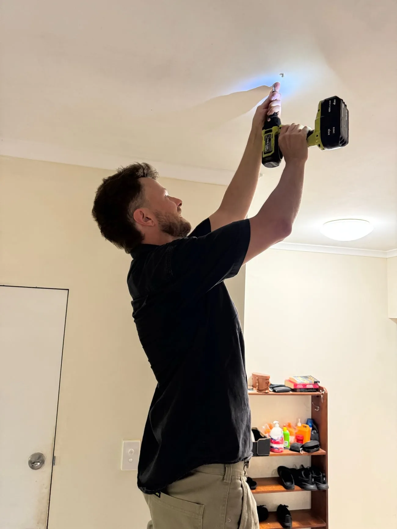 A Reefline electrician working on a ceiling with a drill