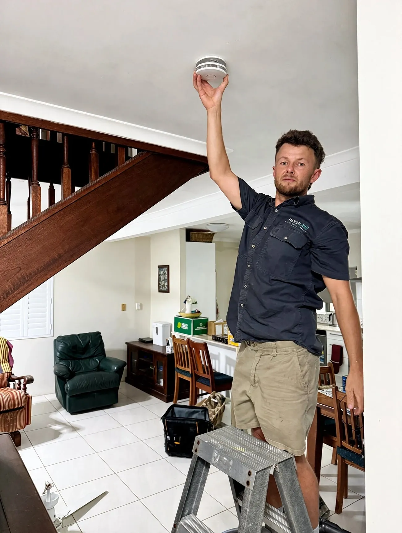 A Reefline electrician holding a smoke alarm up to a ceiling