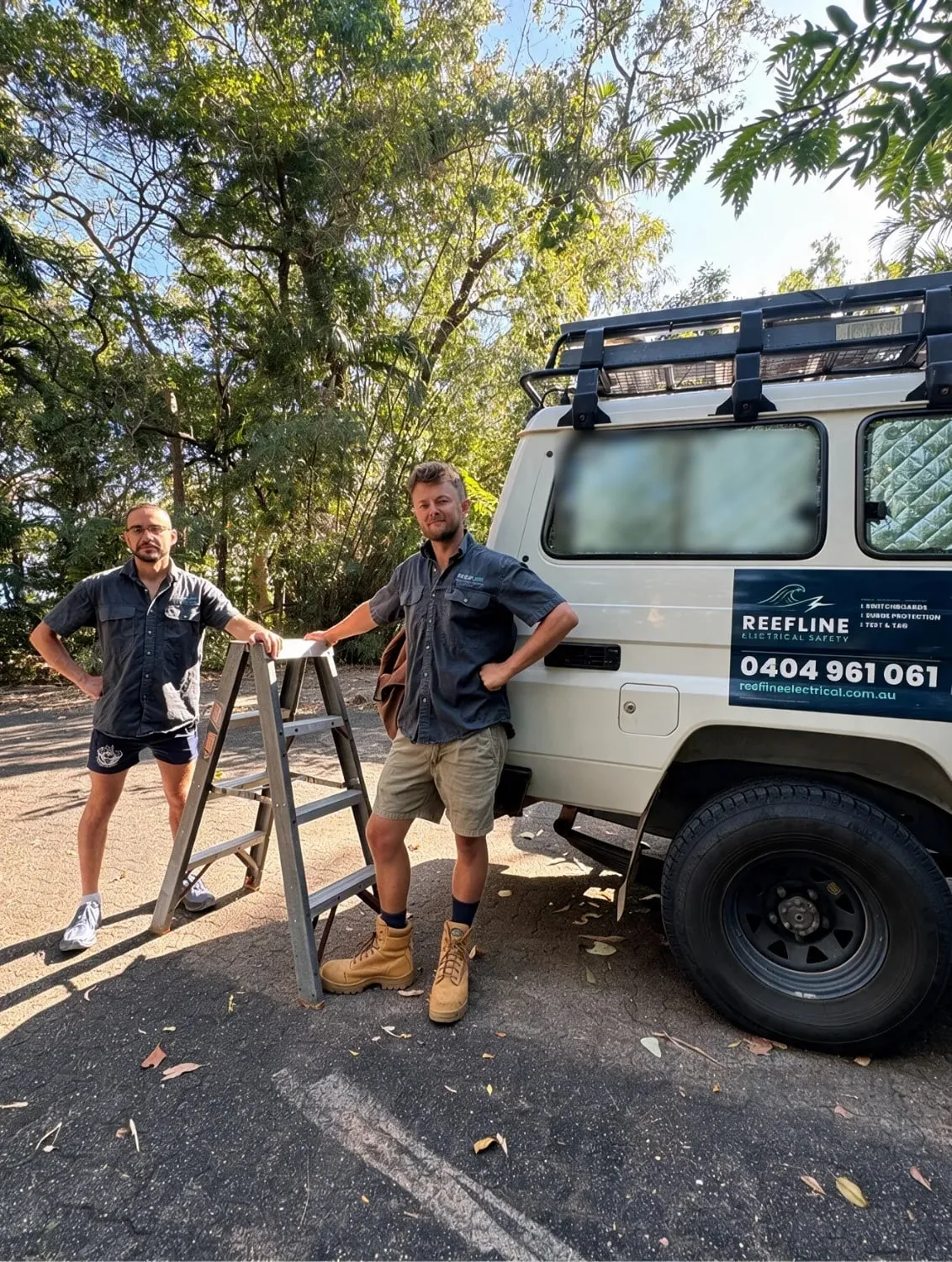 Two Reefline electricians standing beside the work ute with a ladder